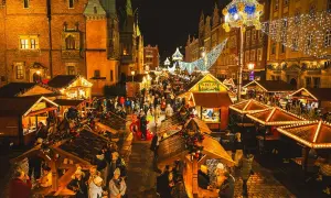 Tłoczny wrocławski jarmark bożonarodzeniowy nocą, rozświetlony tysiącami lampek. Ludzie spacerują między drewnianymi straganami, ciesząc się świąteczną atmosferą.