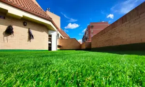 Un vibrante césped artificial para parques infantiles cubre una terraza con edificios de ladrillo y un cielo azul brillante.