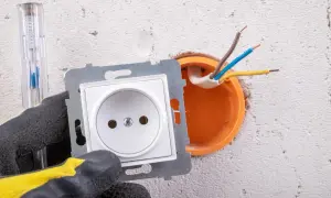 Ręka w rękawicy przygotowuje podłączenie gniazdka. Widać przewody wychodzące z puszki instalacyjnej.