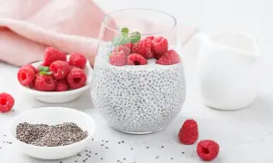 Pudding chia z malinami i miętą w szklance, obok miseczki z nasionami chia i malinami.