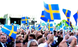 Stor folkmassa viftar med svenska flaggor. Många är lediga på nationaldagen och firar tillsammans.