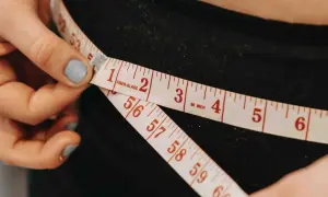 Dłoń z miarką krawiecką pokazuje, jak zmierzyć talię. Widać centymetry i liczby.