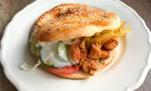 Kebab w bułce z kurczakiem, frytkami, warzywami i sosem na białym talerzu.