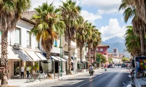 Strada alberata con palme, negozi e gente. Chissà quanto costa una casa qui, con questo panorama.