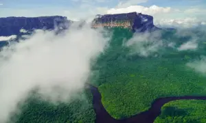 Majestatyczne góry otoczone chmurami, z zieloną dżunglą i krętą rzeką poniżej. Widok przypomina salto angel.