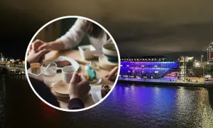 Para trzymająca się za ręce przy stoliku z kawą i ciastkiem, na tle nocnego Szczecina z oświetloną budowlą nad wodą.