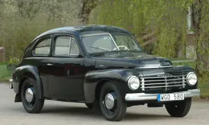 Svart Volvo PV 1954, en klassisk svensk bil, parkerad utomhus med grönska i bakgrunden.