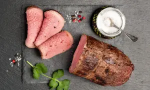 Una succulenta lombata di vitello, affettata e pronta per essere gustata, con sale grosso, pepe e un rametto di coriandolo.