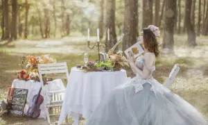 Panna młoda w sukni ślubnej czyta książkę przy stole z owocami i kwiatami. Obok skrzypce i tablica z napisem "We are getting married".
