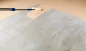 Application d'une peinture claire au rouleau sur un sol en béton, transformant l'espace pour peindre un parquet stratifié.