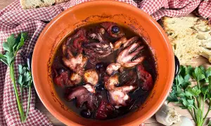 Polipetti alla luciana in terracotta, con pomodoro, olive e pane tostato.