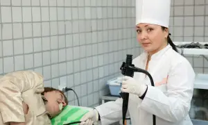 Lekarka w białym kitlu przygotowuje pacjenta do gastroskopii, trzymając endoskop.