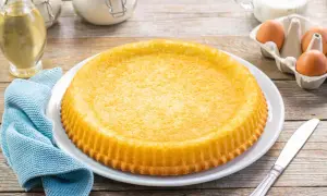 Una torta furba dorata, appena sfornata, su un piatto bianco. Ingredienti come uova e olio sono visibili sullo sfondo.
