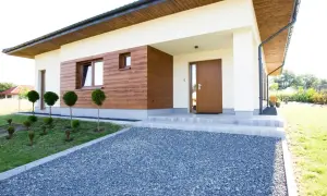 Nowoczesny dom z jasnym tynkiem, drewnianą elewacją imitującą tynk kornik i brązowymi oknami.