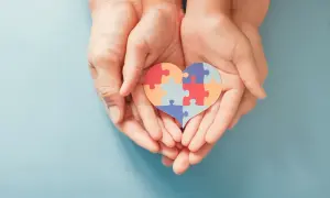 Dłonie trzymają serce z puzzli, symbolizujące wsparcie dla osób z autyzmem i ich unikalne wokalizacje.