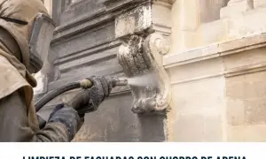 Restauración de fachadas con limpieza a chorro de arena. Un operario con equipo de protección limpia detalles ornamentales de piedra.