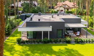 Nowoczesne projekty domów do 100m2 w otoczeniu lasu. Elegancki, ciemnoszary budynek z płaskim dachem i dużymi przeszkleniami.