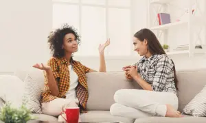 Dwie kobiety siedzą na kanapie, rozmawiając. Jedna z nich gestykuluje, pokazując różne techniki komunikacji interpersonalnej.