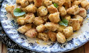 Bocconcini di pollo dorati e croccanti, guarniti con scorza di limone e foglie di menta fresca su un piatto decorato.