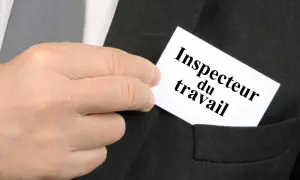 Main d'un homme glissant une carte "Inspecteur du travail" dans la poche d'un costume.