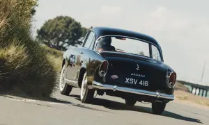 Svart Simca Aronde glider längs en kustväg, en klassisk skönhet bland gräs och träd.