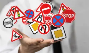 Main de personne tenant une multitude de panneaux de signalisation routière, dont certains indiquent la signification panneau interdiction poids lourds.