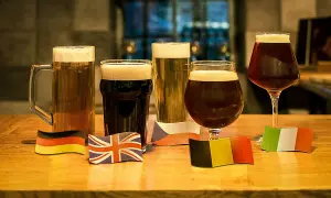 Cinque bicchieri di birre scure famose, ognuno con una bandiera nazionale: Germania, Regno Unito, Repubblica Ceca, Belgio e Italia.