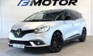 En silverfärgad Renault Grand Scénic med svarta fälgar står framför en vägg med logotypen B MOTOR.