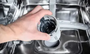 Ręka wyjmuje filtr zmywarki, który może być przyczyną, że zmywarka nie domywa.