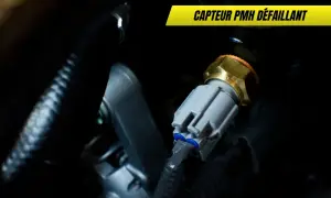 Capteur PMH défaillant : un composant moteur avec un connecteur gris et un corps hexagonal doré, entouré de câbles noirs.