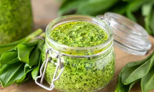 Słoik pełen aromatycznego pesto z czosnku niedźwiedziego, otoczony świeżymi liśćmi tej wiosennej rośliny.