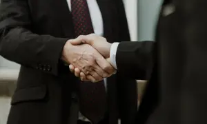 Dwaj mężczyźni w garniturach ściskają sobie dłonie. To symbol porozumienia, jak w art. 180 kpk.