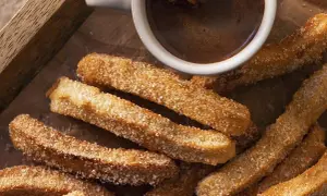 Churros caseros espolvoreados con azúcar junto a una taza de chocolate caliente.