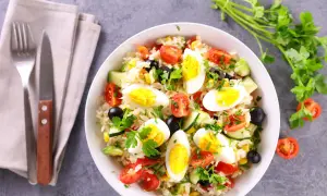 Una gustosa insalata di riso con uova sode, pomodorini, olive, mais e cetrioli, guarnita con prezzemolo fresco.
