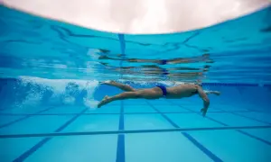 Underwater view of a swimmer performing flutter kicks, propelling through the blue pool water.
