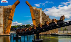 Ekipa rollercoastera w Energylandii gotowa na przygodę! Drewniane wagoniki pędzą nad wodą, a za nimi widać fioletowe tory.