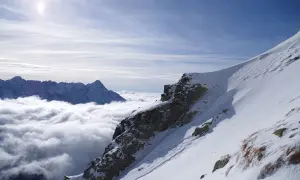Śnieżne zbocze Kozi Wierch, z chmurami poniżej i skalistymi szczytami w oddali.