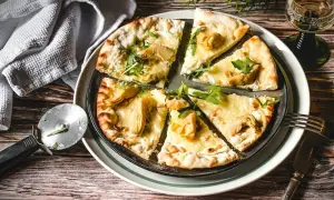 Eine köstliche Pizza Bianca mit Artischocken, Rucola und Pinienkernen, bereit zum Genießen.