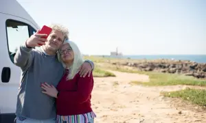 Para singli po 50-tce, którzy szukają przygód, idealne są wycieczki kamperem. Para robi sobie selfie na tle morza.