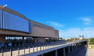 Nowoczesny budynek lotniska Aeropuerto de Menorca z napisem "AEROPUERTO DE MENORCA" i podjazdem pod niebo.