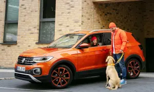 Pomarańczowy mini suv z kobietą w środku i mężczyzną z psem na smyczy.