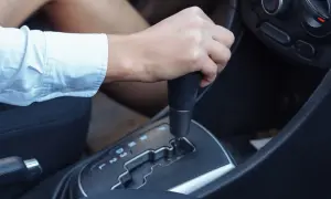 Dłoń na dźwigni zmiany biegów, widoczne oznaczenia automatycznej skrzyni biegów: P, R, N, D, 3, 2, L.