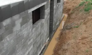 Budowa fundamentów z bloczków betonowych, obok wykop z wodą, który wymaga drenażu.
