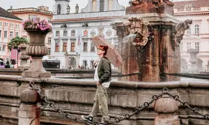 Regenschirm-Schwung am Brunnen in Budweis Stadt. Die Frau genießt die frische Brise, während die historische Kulisse im Hintergrund erstrahlt.