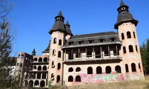 Niedokończony zamek w Łapalicach, z ceglanymi wieżami i arkadowymi balkonami, pokryty graffiti, pod błękitnym niebem.