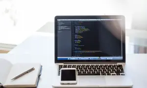 Laptop z kodem, telefonem i notatnikiem. Dobry laptop powinien mieć odpowiednie parametry do pracy.