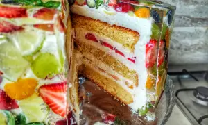 Kolorowy tort z galaretką i owocami, przekrojony, ukazujący warstwy biszkoptu i kremu.