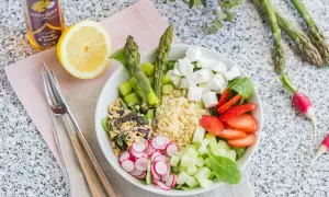 Un plat végétarien coloré avec du quinoa, des asperges, des fraises, du concombre, des radis, des graines et du fromage feta.
