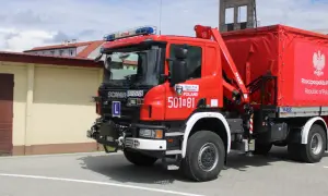 Czerwony strażak OSP Scania z żurawiem i plandeką z godłem Polski gotowy do akcji.