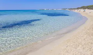Spiaggia di Punta Prosciutto, Maldive del Salento. Acque cristalline e sabbia dorata sotto un cielo azzurro.